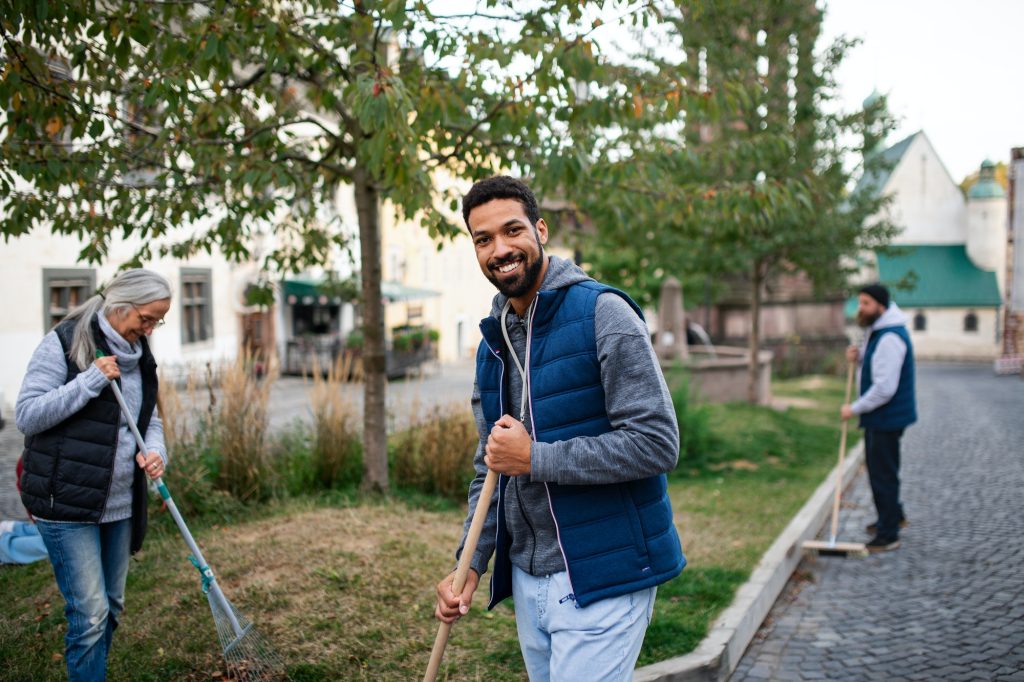 Young man volunteer with team looking at camera and cleaning up street, community service concept