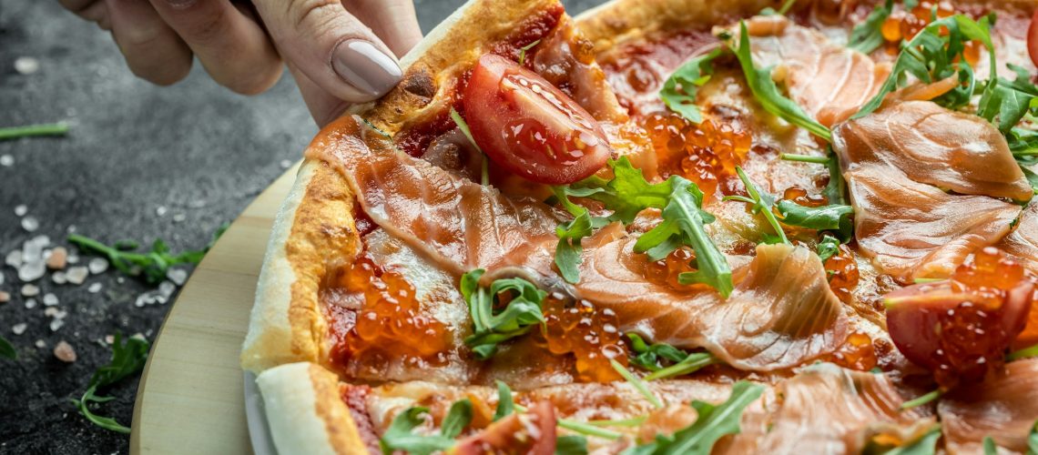 Female hands holding delicious pizza with salmon, red caviar, tomatoes and aragula. italian pizza